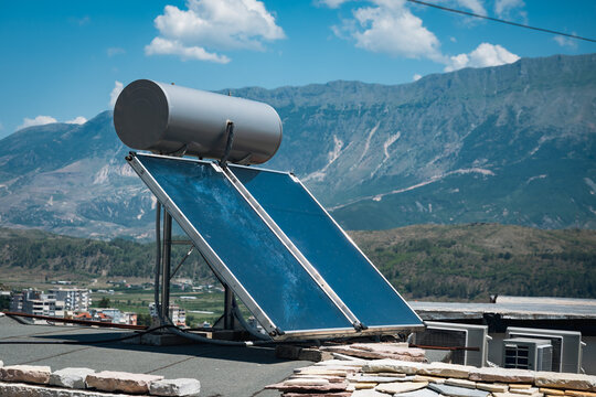 Solar water heating system and photovoltaic panels installed on rooftop with mountain landscape, showcasing renewable energy and sustainable technology under blue sky
