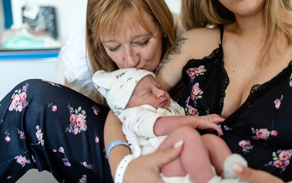 Grandmother kissing new born baby held by mother