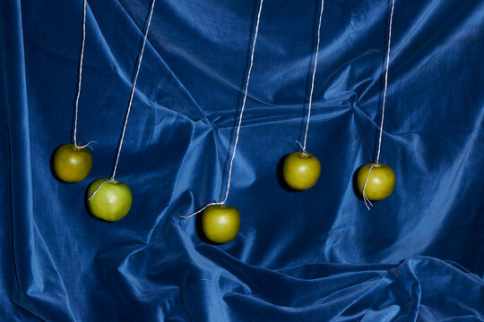 Five Green Apples Swing Against a Blue Velvet Background