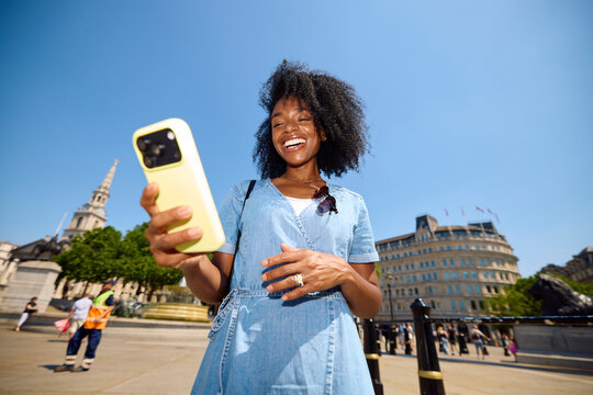 Woman smiles as she uses her phone in a city square