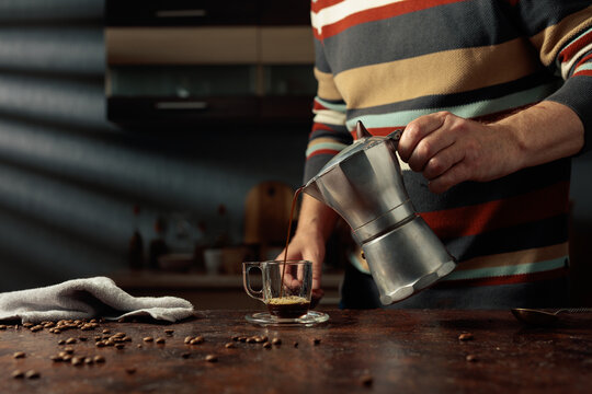 A man in a striped sweater is poured coffee from a geyser coffee maker into a glass cup.