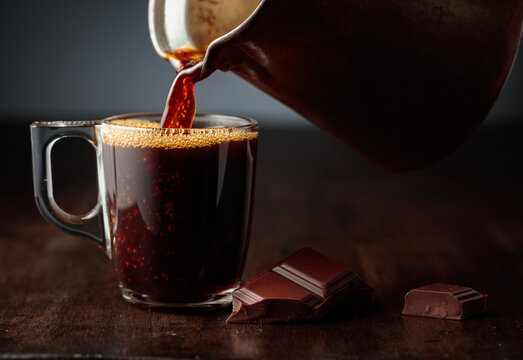 Black coffee is poured into a glass cup.