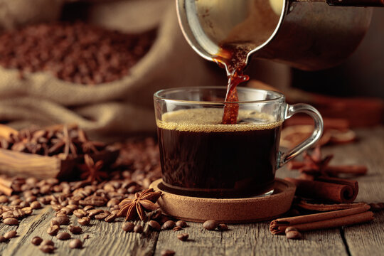 Black coffee is poured from a copper coffee pot into a glass cup.