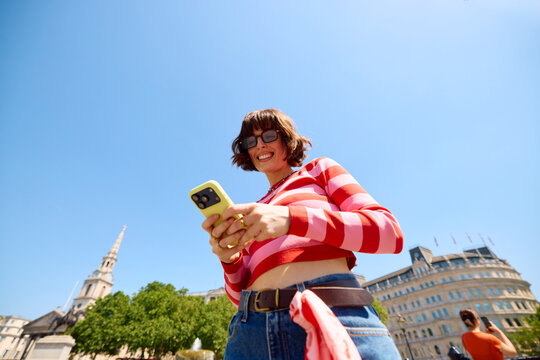Woman Smiles While Using Phone in City Square on a Sunny Day