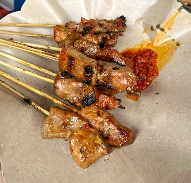 Indonesian traditional grilled chicken ,known as sate or satay, served on oil paper with spicy red chili sambal.