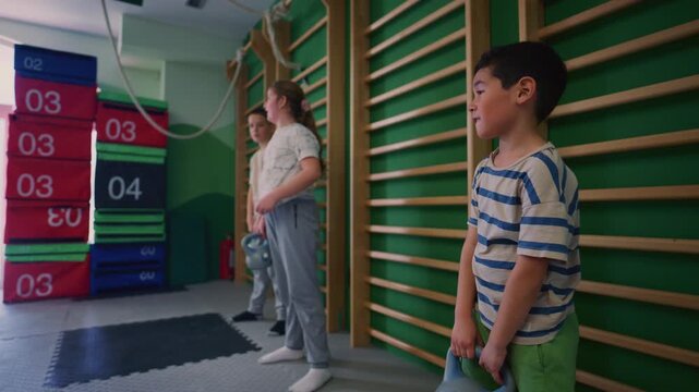 Young children are seen actively participating in a fitness exercise, lifting kettle bells. These kids demonstrate strength and concentration during their gym workout.