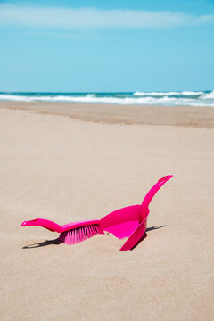 a pink dustpan and brush rest half buried on the sand