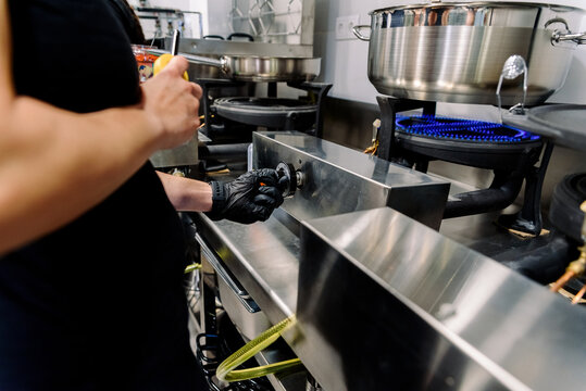 A chef wearing gloves works with cooking equipment in a busy restaurant kitchen preparing meals for customers during dinner service
