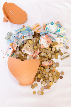 Terracotta piggy bank overflowing with euro banknotes and coins