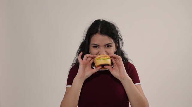 Happy young woman holding a fake burger and pretending to eat