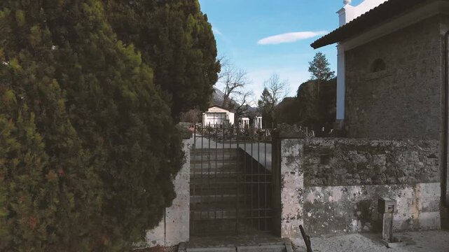 Horizontal 4K 30fps aerial video of a drone taking off vertically from the ground in front of an old church. Panoramic view of a river valley and mountains under a clear blue sky