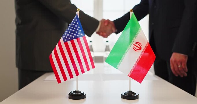 Handshake diplomacy agreement negotiation treaty by diplomats. USA and Iran flags stand by documents during cordial meeting. Symbolizes international politics diplomacy and bilateral agreement.