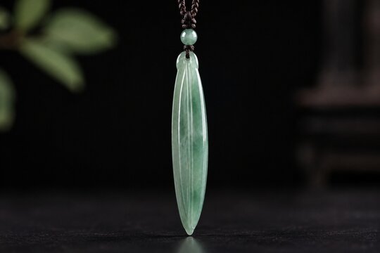 A slender green jade pendant shaped like a silique on a dark background.
