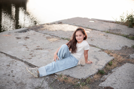 A young girl of Hispanic descent sits casually on a sunlit dock, showcasing her relaxed style and playful spirit.