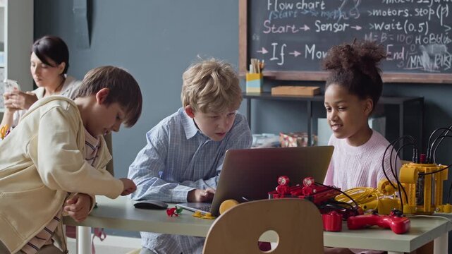 Diverse children, including Caucasian boys and Black girl, collaborating on robotics coding project using laptop in classroom. Footage is perfect for STEM education marketing