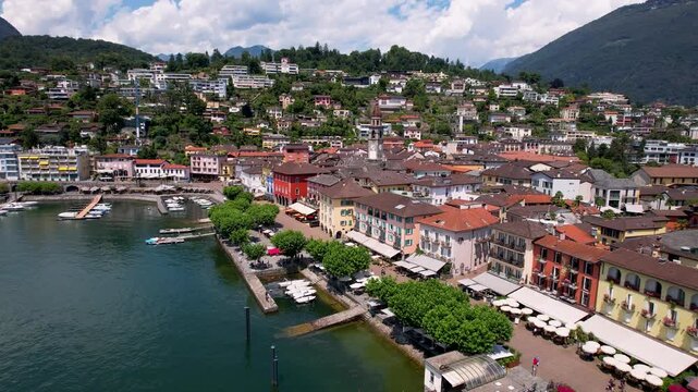 Ascona Lake Maggiore Switzerland 4K Drone. Aerial view of clock tower bell tower with colorful houses and boats on water. Ticino canton travel scenic destination b roll cinematic video