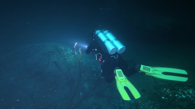 Scuba diver with a flashlight exploring a dark underwater cave in a cenote