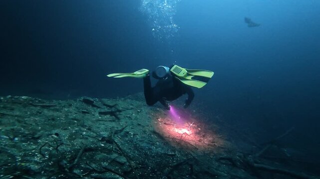 Scuba diver with a flashlight exploring the mysterious dark waters of an underwater cave in a cenote