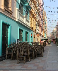 Obraz premium Stacked wooden chairs in front of vibrant colorful shop on sunny city street scene.