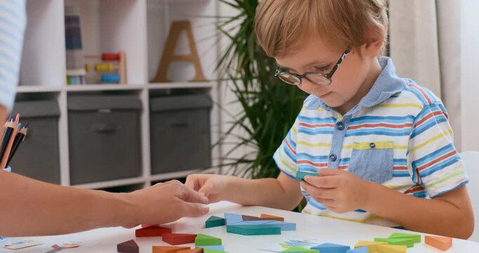 Young boy with glasses doing crafts at table in classroom, collage of video frames