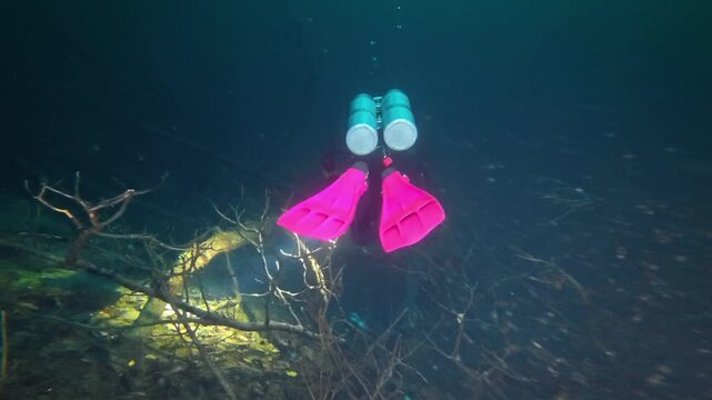 Scuba diver with bright pink fins swimming through a dark, underwater cave system in a cenote