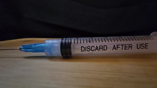 A close-up view of a medical syringe with a blue needle tip resting on a wooden surface, highlighting clinical precision and healthcare equipment.