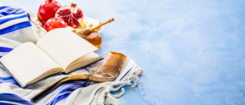 Rosh Hashanah arrangement with open book, apples, honey, and shofar on blue background. banner format