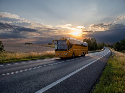 A yellow bus driving on the asphalt road winding through idyllic rural landscape during mystical sunset