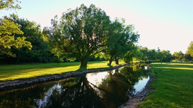 Serene canal reflects golden dusk light beneath lush willow trees at Ann Morrison Park in Boise Idaho