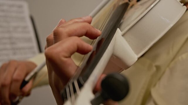 Extreme close-up shot of unknown girl playing violin, pressing fingers on fingerboard while practicing with sheet music in blurred background. Clip for music education ads and online tutorial promos