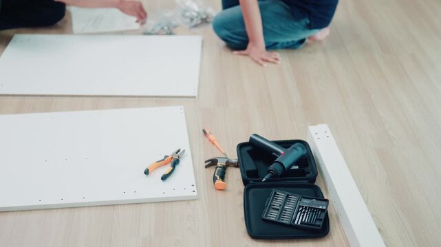 Person Assembling Flat Pack Furniture on Floor with Drill, Pliers, Hammer and Screwdriver Bit Set