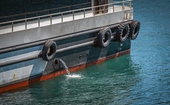 water from a ship to cool the engine, discharge. Outflow of ballast water from ship. Shock absorbing truck tires hanging on the side of the ship.