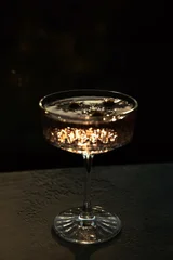 A crystal coupe glass filled with a cocktail catches bright golden light with dramatic light reflections on a dark background. Luxury drink, night party mood, mysterious atmosphere © magic_cinema