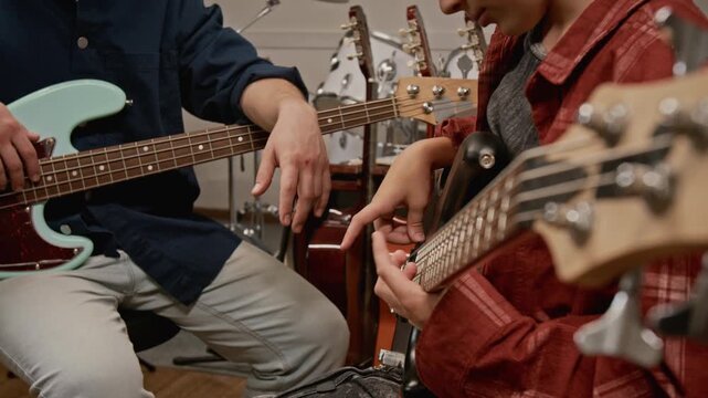 Midsection shot of unknown music teacher instructing child on playing bass guitar in studio. Footage for music school promotions and educational ads