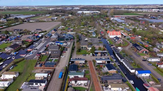 Aerial wide angle view of a scenic marina canal inside a holiday village park with parked boats yachts speedboats and recreational houses under a bright spring sky