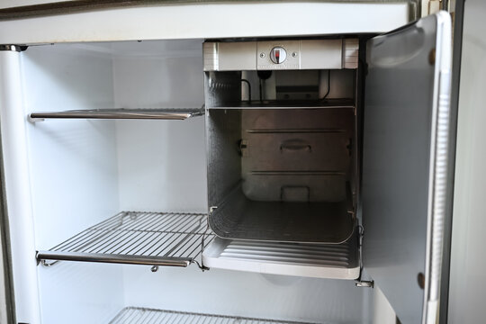 Interior view of an empty vintage refrigerator with wire metal shelves and built-in freezer compartment