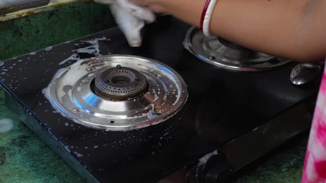 Close up of woman hand washes using a microfiber cloths with foam cleaning stainless steel gas stove in the kitchen. ensuring hygienic and cleaning maintenance concept.