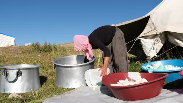A woman transfers fresh cheese curds from a large metal pot into a cloth-lined container, showing traditional cheesemaking, manual dairy work, and small-scale outdoor food production outdoors by hand.