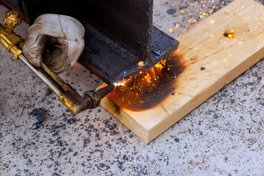 Worker uses welding tool to join metal pieces on wooden surface in outdoor setting