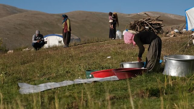 A woman squeezes a cloth bag of fresh curds over a red basin, showing a traditional cheese-making stage, manual whey draining, rural food preparation, and small-scale outdoor dairy production by hand.