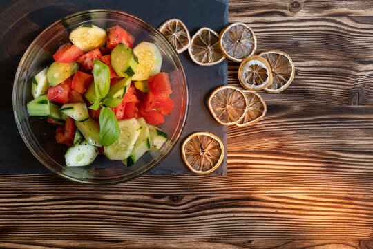 Fresh tomato and cucumber salad with dried citrus on a slate and wooden background