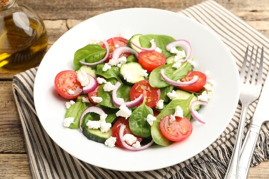 Appetizing spinach salad with cheese, walnuts and vegetables served on wooden table, closeup