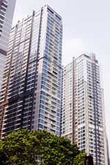 Fototapeta premium Two tall modern residential skyscrapers rising behind green trees under a bright sky in Saigon. urban real estate growth, luxury apartment towers.