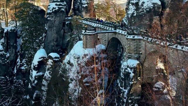 Famous Bastei Bridge in winter with tourists walking. Snow covered landscape in Saxon Switzerland National Park, Germany. Travel and nature concept. 