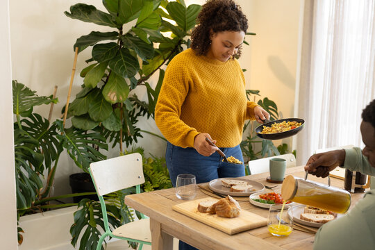 African American couple preparing meal at dining table with frying pan, spatula, pitcher