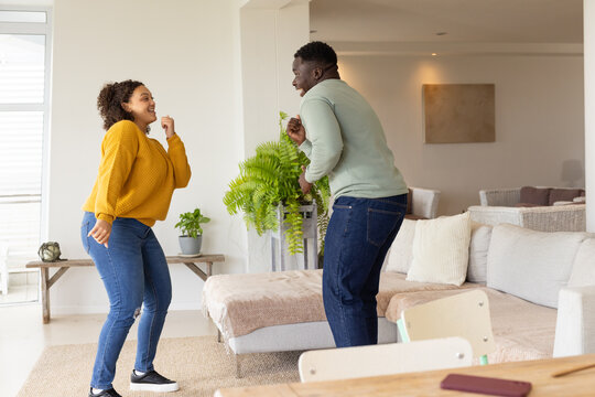 African American couple dancing at home near potted fern wearing mustard sweater and green top