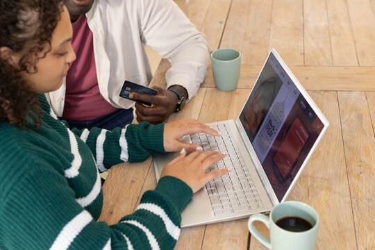 African American couple typing on laptop, holding credit card at dining table with mint green mugs
