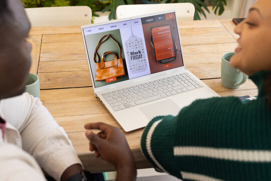 Diverse friends reviewing Black Friday storefront on white laptop at home one wearing green sweater
