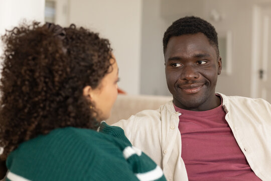 Couple talking on beige couch at home, man wearing maroon tee facing woman in green sweater