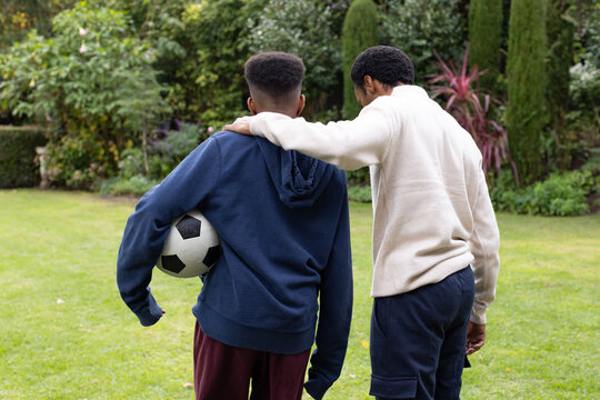 African adult and teen males walking in yard wearing sportswear holding b and w soccer ball and obje